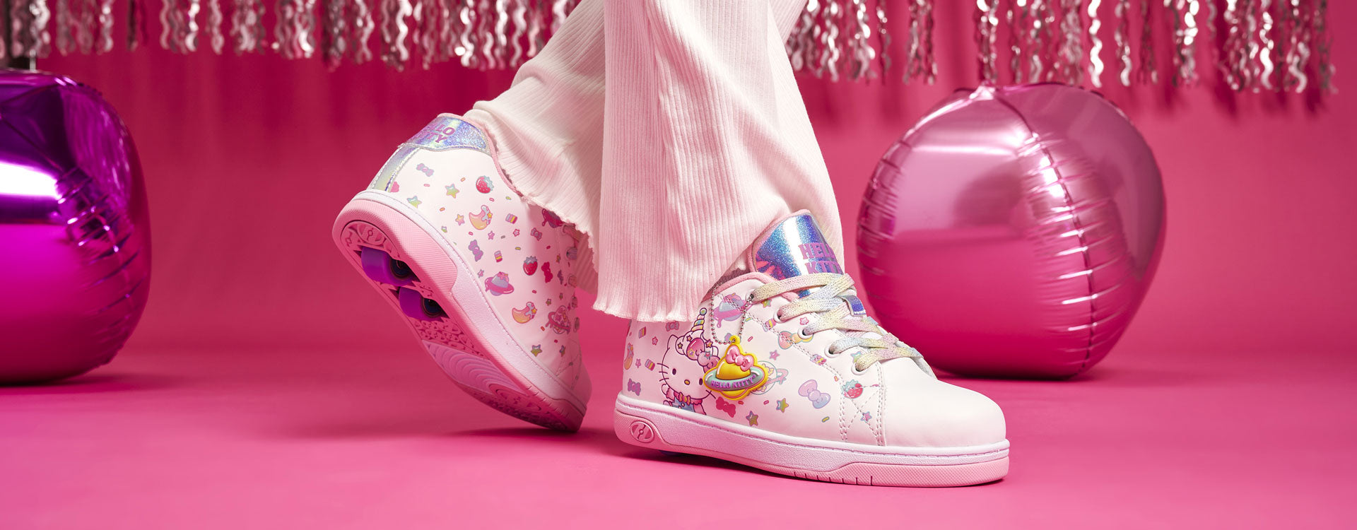 White Hello Kitty Heelys roller shoes with colorful design on a pink background