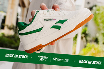 White Reebok Heelys roller shoe with green accents held by a hand, with a 'Back in Stock' banner at the bottom.