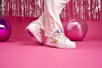 White Hello Kitty Heelys roller shoes with colorful designs worn on a pink background