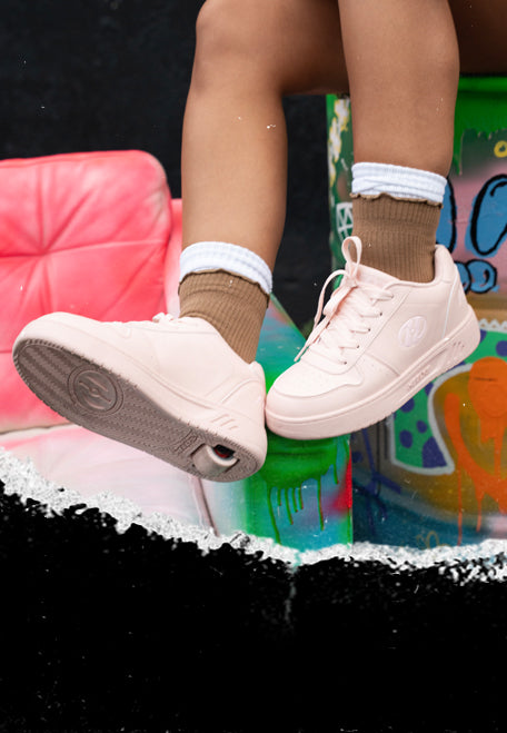 Girls Heelys roller shoes. Person wearing light pink Heelys wheeled shoes with white soles, sitting on a colorful barrel.