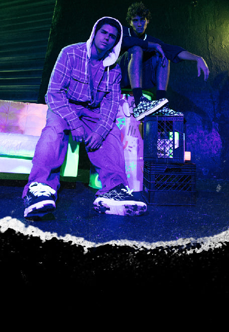 Men's Heelys Roller Shoes. Two people sitting in a dark room with neon lighting, wearing Heelys wheeled shoes.